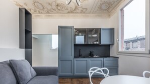 A modern living room with a grey sofa, a white dining table, and a kitchen with grey cabinets and a window. - L'Altana di Emilia Suite (Modena)