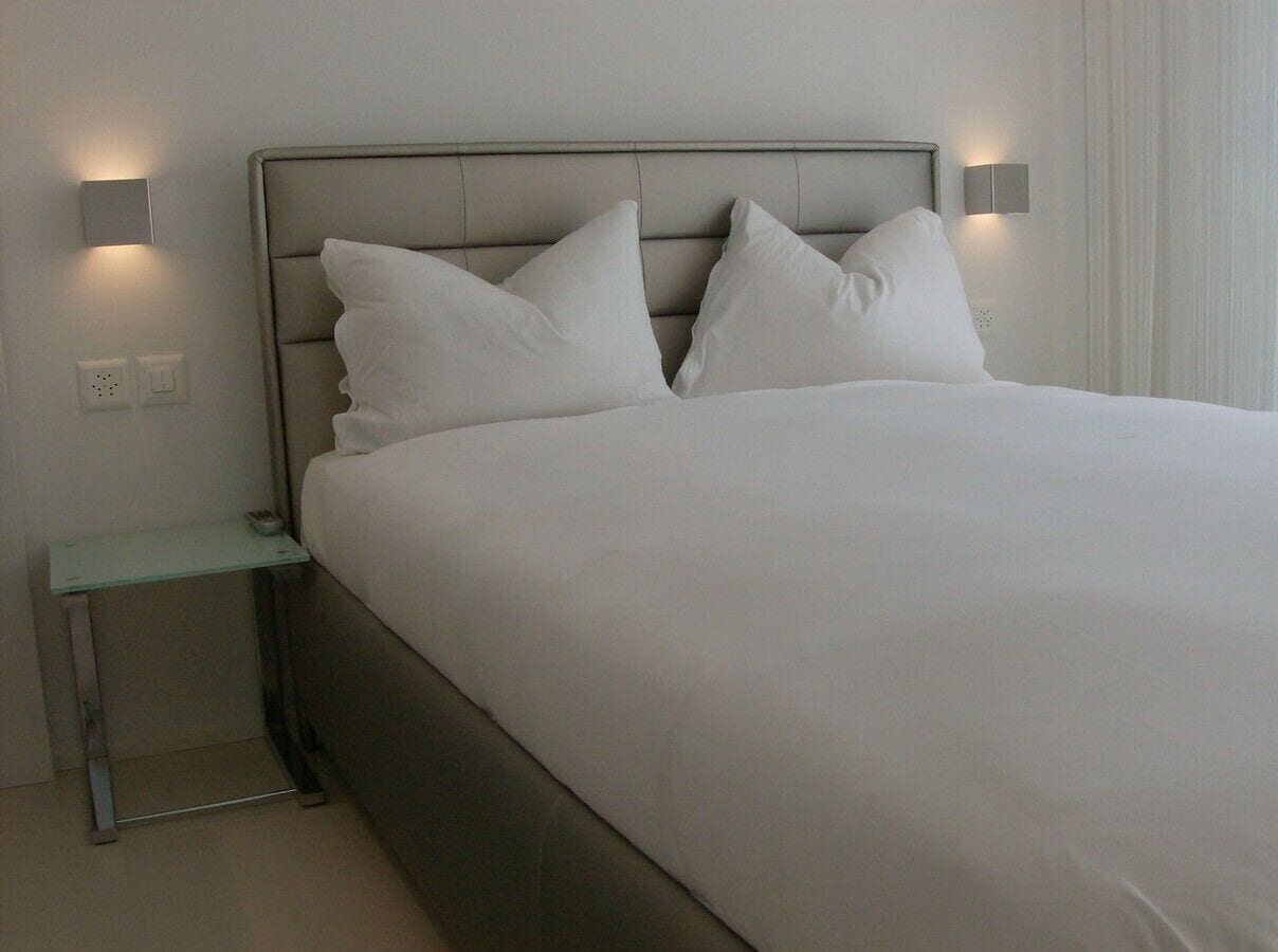 A modern hotel room with a large bed, two bedside tables, and wall-mounted lighting.