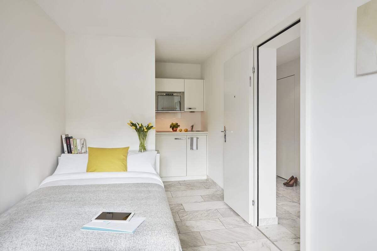 A bedroom with a bed, a bedside table, a nightstand, a window, and a door leading to a bathroom.