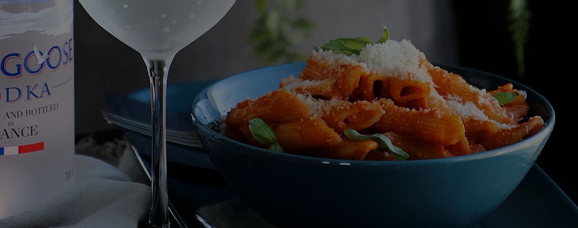 A bowl of pasta with a glass of water and a bottle of Gocase DKA.