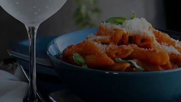 A bowl of pasta with a glass of water and a bottle of Gocase DKA.