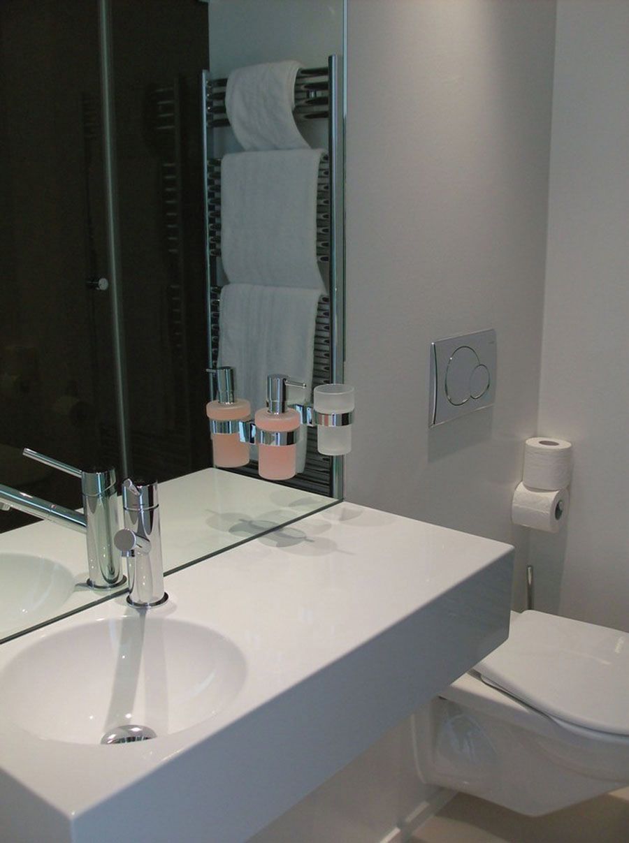 Une salle de bain moderne avec un lavabo blanc, des robinets chromés, un miroir et des toilettes.