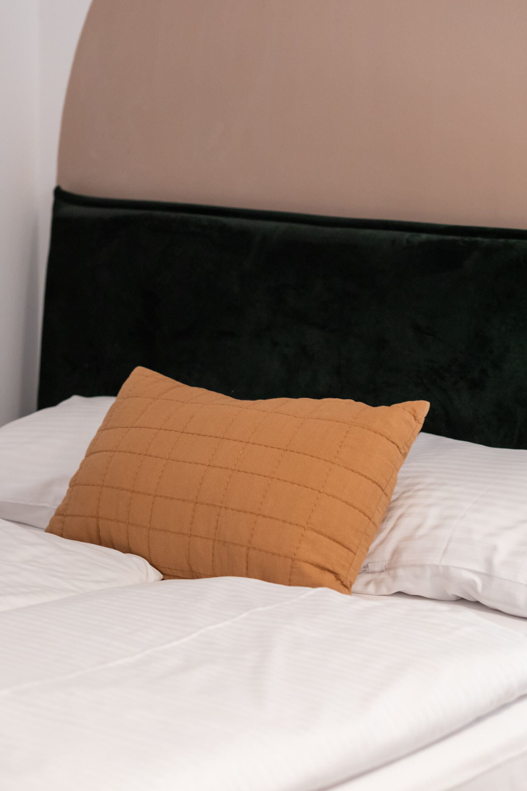 A bed with white bedding and a single mustard-colored pillow.