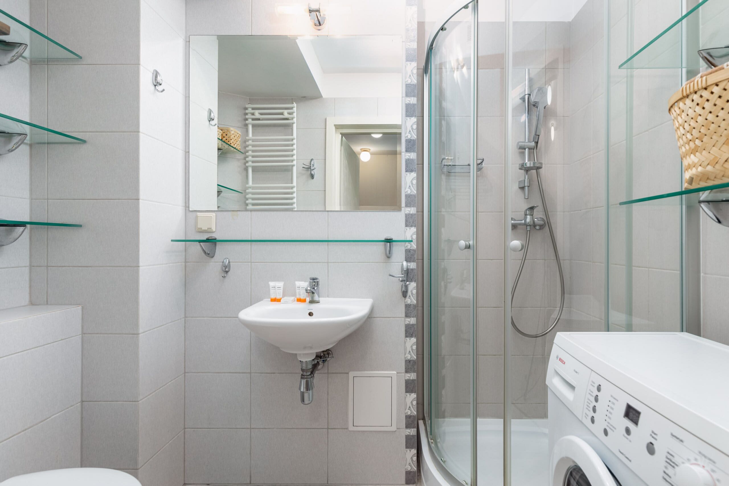 A modern bathroom with a glass shower enclosure, a white sink, and a built-in washing machine.