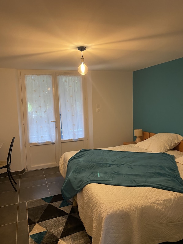 A bedroom with a bed, a window with curtains, a lamp, and a geometric-patterned rug.