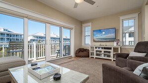 A spacious living room with a large TV, comfortable seating, and a balcony with a view of buildings.