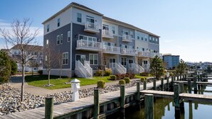 A multi-story residential building with balconies, a dock extending into a body of water, and a well-maintained lawn.