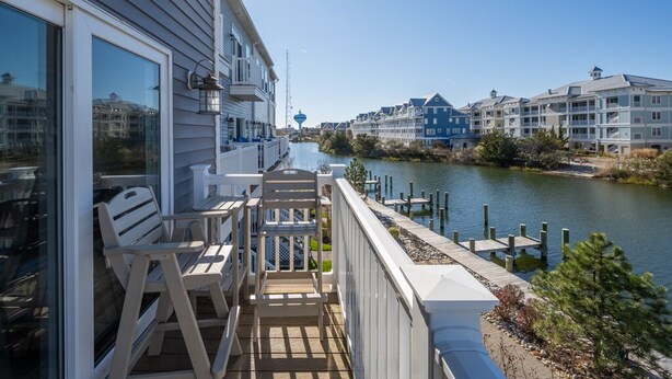 A balcony with outdoor seating, overlooking a river with buildings in the background.