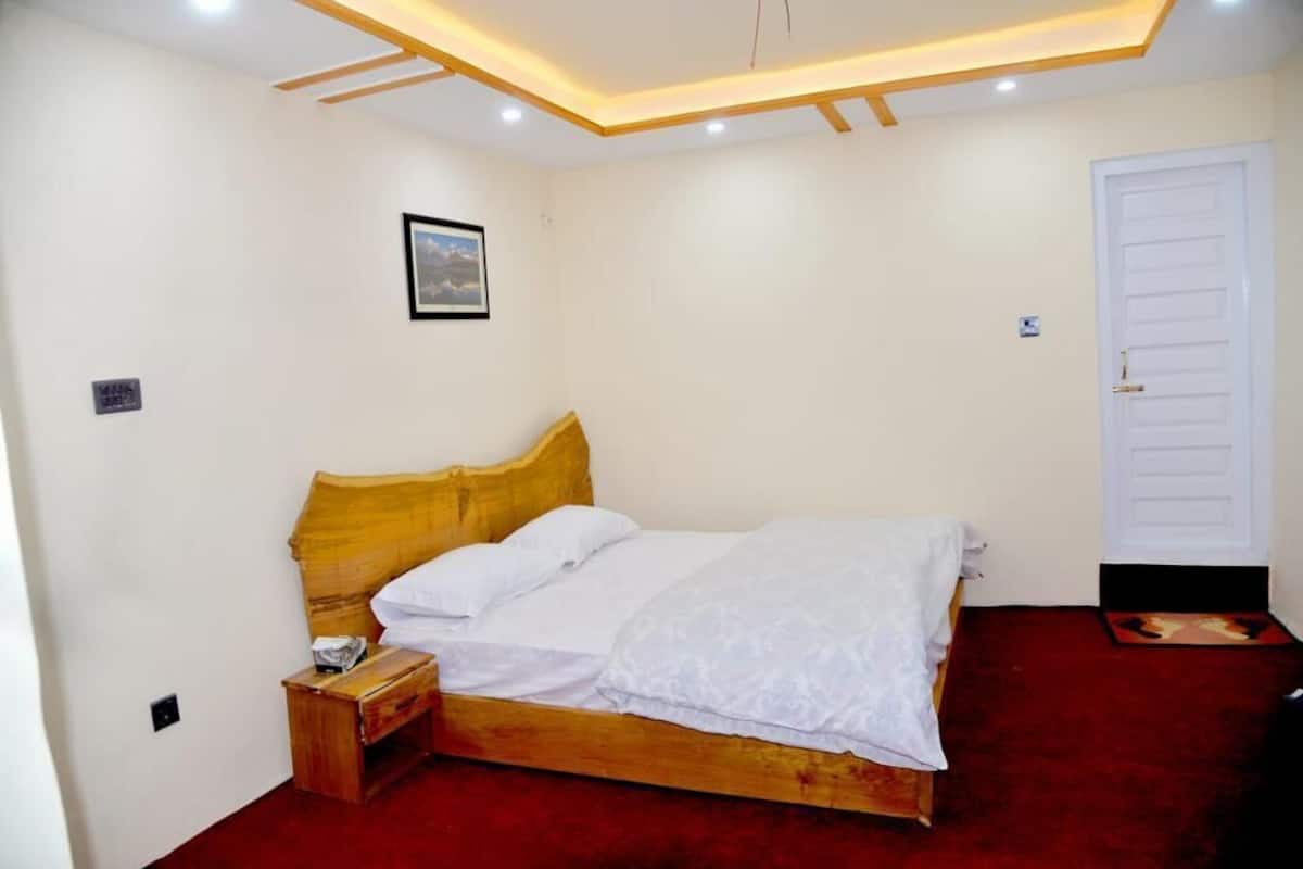 A bedroom with a wooden bed, white bedding, a nightstand, a framed picture on the wall, and a white door.