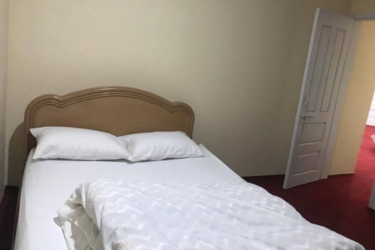 A bed with a wooden headboard, white bedding, and a closed door to the right.