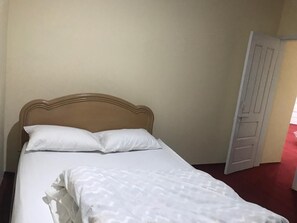 Una cama con cabecera de madera, ropa de cama blanca y una puerta cerrada a la derecha.