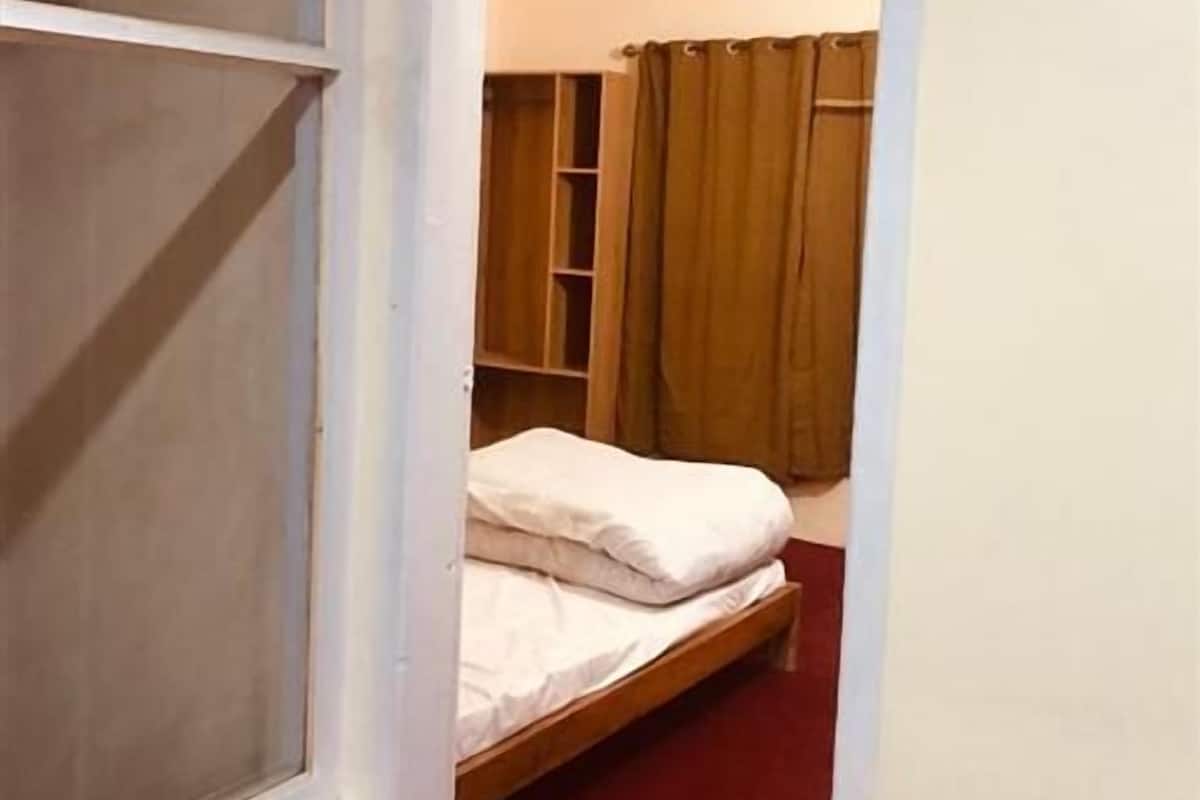 A narrow hallway leading to a bedroom with a bed, a wardrobe, and a window.