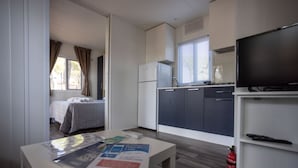 A compact hotel room with a kitchenette, a bed, a small table with brochures, and a television. - Anxur Village Camping (Fondi)