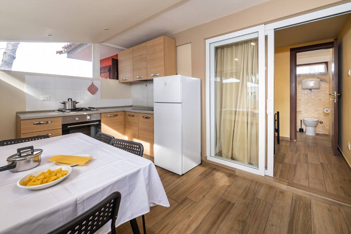 Eine moderne Küche mit Holzschränken, einem weißen Kühlschrank und einem Esstisch, gedeckt mit Pasta.