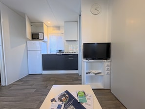 A modern kitchen with a microwave, stove, and cabinets, a flat-screen TV on a stand, and a clock on the wall.