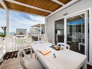 A covered outdoor dining area with a white table, chairs, and a view of the sea. - Anxur Village Camping (Fondi)