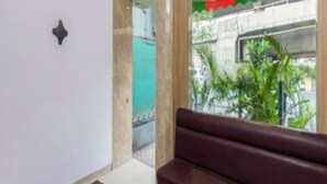 A modern interior with a bench, a small rug, and a view of a street with greenery and a building. - Panvel Palace (Panvel)