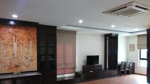 A spacious living room with a large painting, a flat-screen TV, and a dining area with chairs and a table. - Capital O 90653 Maxwell Inn Boutique Hotel (Taiping)