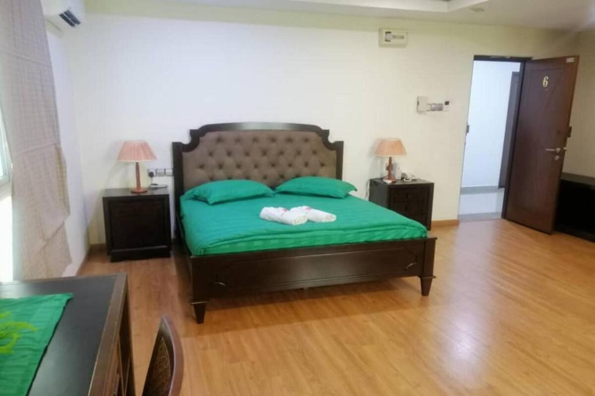 Une chambre à coucher avec un lit en bois, une literie verte, deux tables de chevet avec des lampes et une porte.