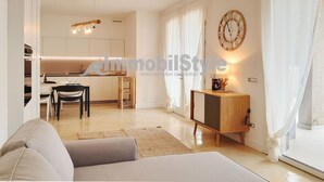 Uma sala de estar moderna com sofá, área de jantar com cadeiras e mesa, cozinha com armários e uma janela grande com cortinas.