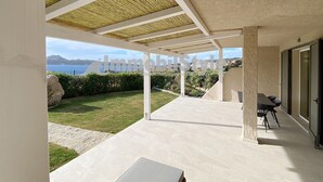 Uma área externa coberta com vista para o mar, uma mesa com cadeiras e um caminho de pedra.