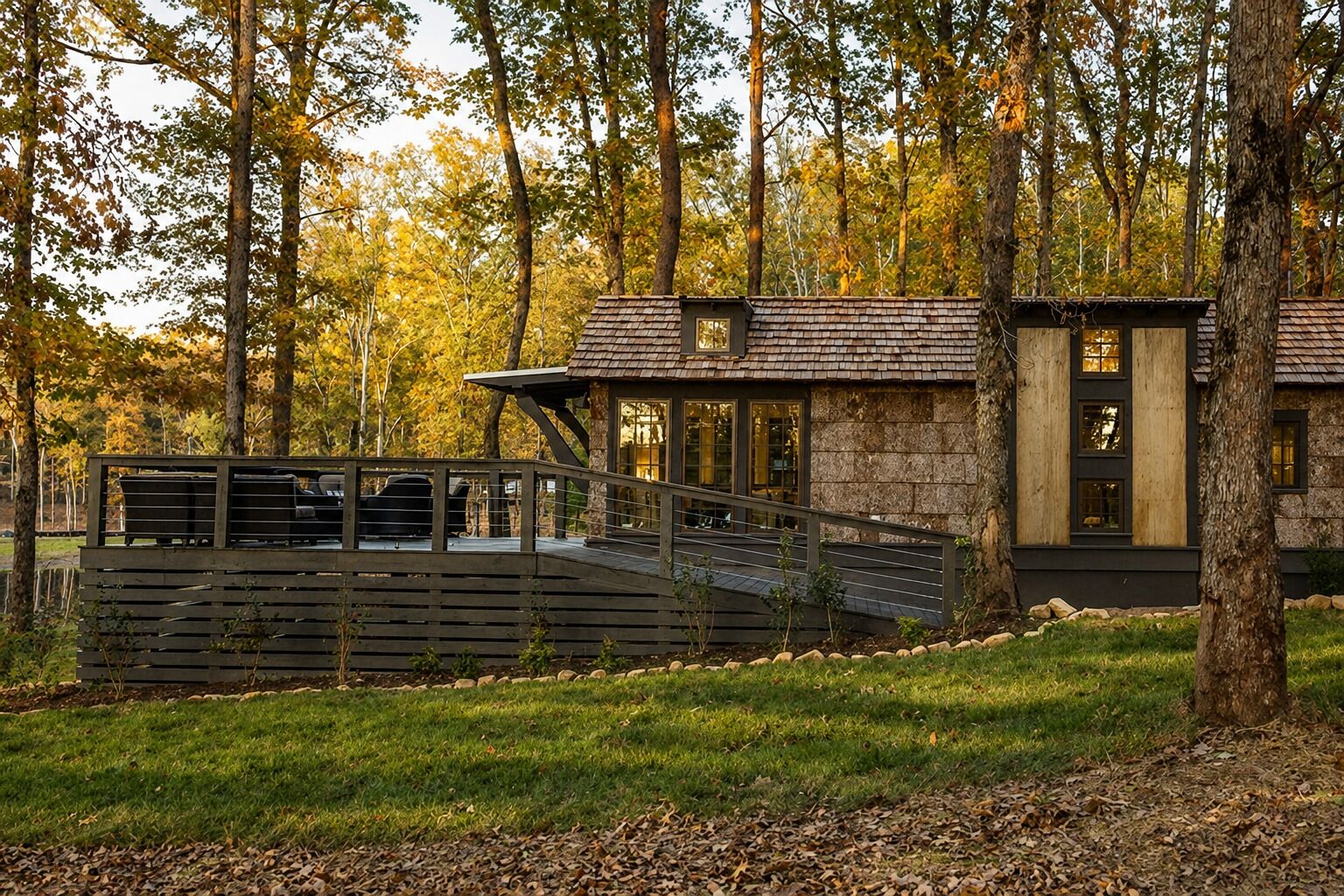 Une cabane moderne avec une façade en pierre, une terrasse en bois et une entrée avec une porte en verre.