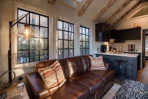 Un salon chaleureux avec un canapé en cuir, des coussins décoratifs à motifs et une grande fenêtre donnant sur une forêt.