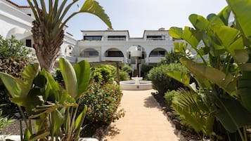 Un camino que lleva a un edificio blanco con arcos y una fuente.