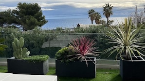 A balcony with potted plants, a view of the sea, and palm trees. - Villa Miami (Roquebrune-sur-Argens)