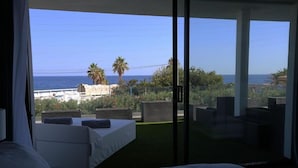A bedroom with a large bed, a balcony with seating, and a view of the sea and landscape. - Villa Miami (Roquebrune-sur-Argens)