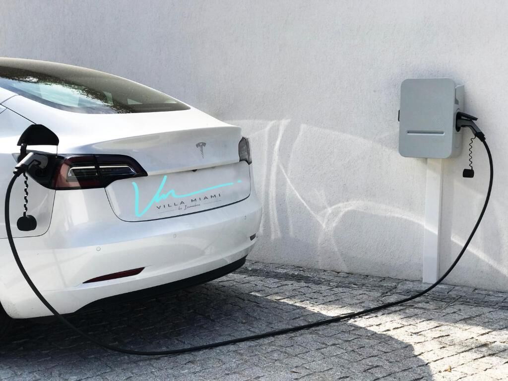 Une voiture électrique blanche est garée à côté d’une borne de recharge.