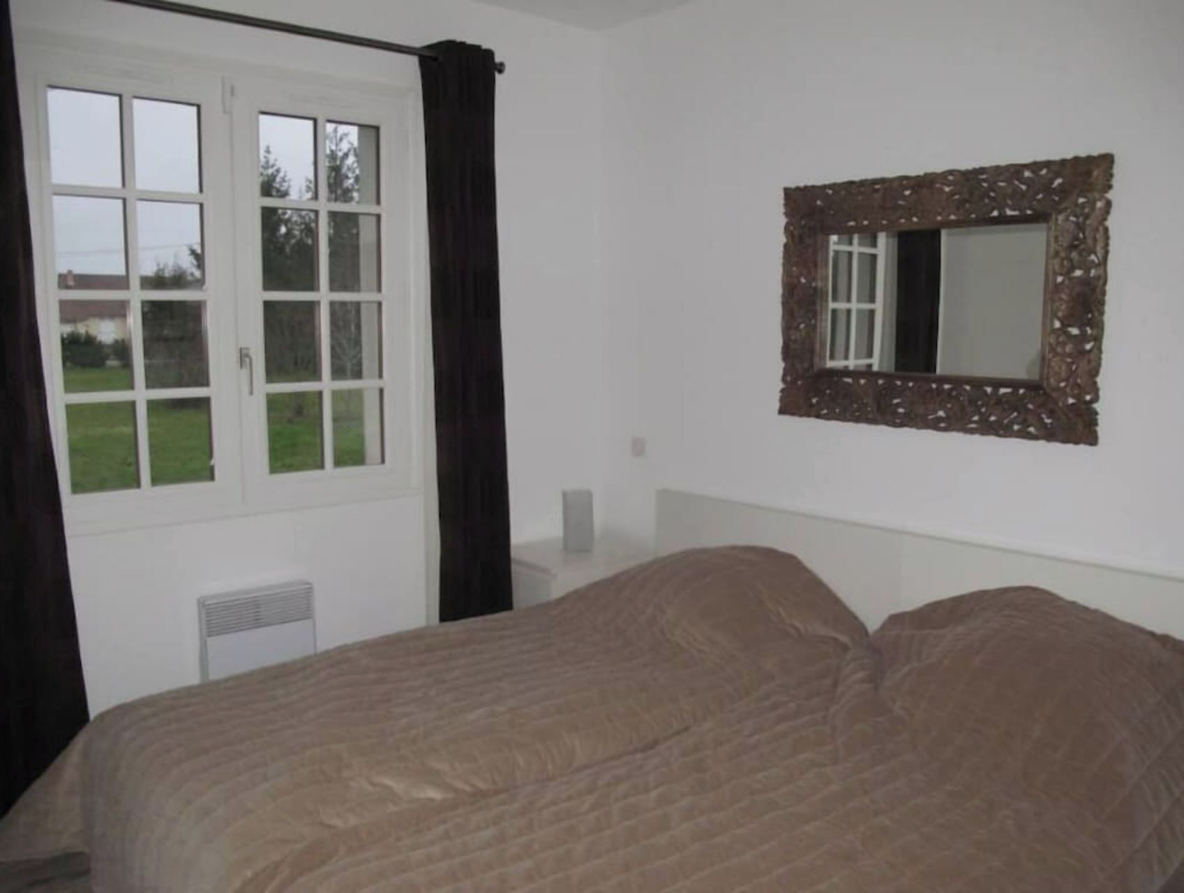 A bedroom with a bed, a window with curtains, and a wall-mounted mirror.