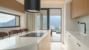 A modern kitchen with a central island, wooden cabinetry, and a view of the city and mountains through large windows. - Nandana Luxury Villa, an infinite blue experience (Rethymno)