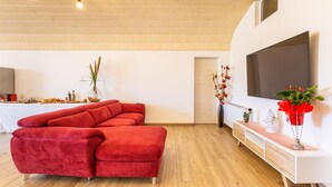 A modern living room with a red sectional sofa, a wooden floor, a white console table, and a large TV mounted on the wall. - 2943 Casa Marangi by Barbarhouse (Ostuni)