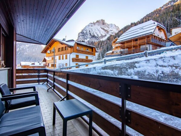 A wooden balcony with benches overlooking a snowy mountain landscape and traditional wooden buildings.