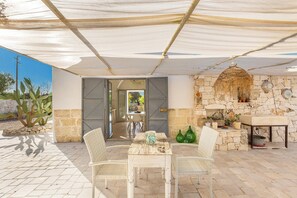 An outdoor patio with stone flooring, a table with chairs, a stone wall with a fireplace, and a hanging light fixture. - 122 Lamia Madreperla by Barbarhouse (Carovigno)