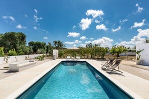 A rectangular swimming pool with clear blue water, surrounded by a tiled deck. There are two lounge chairs on one side of the pool.