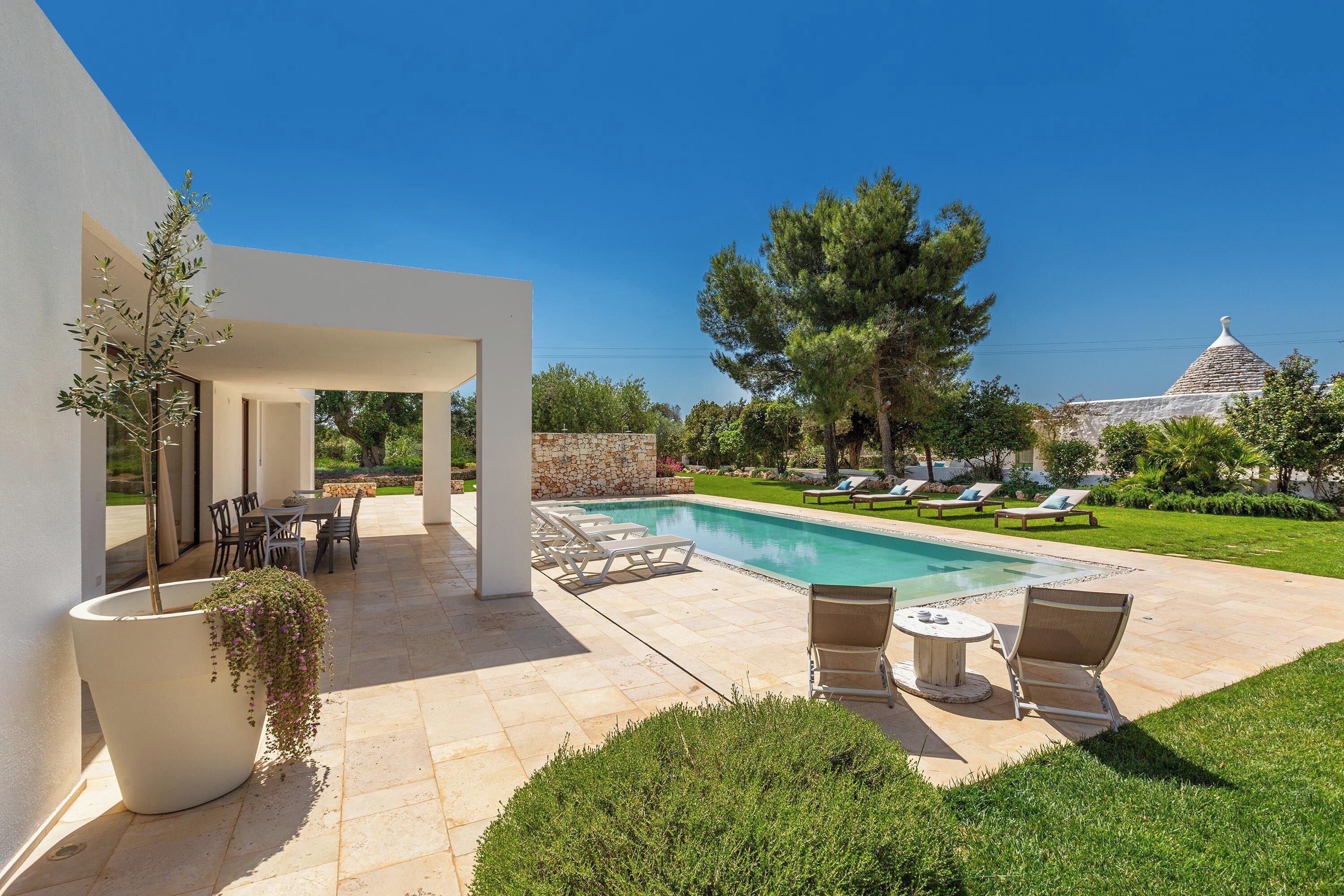 A modern outdoor pool area with a stone wall, lounge chairs, and a dining area.
