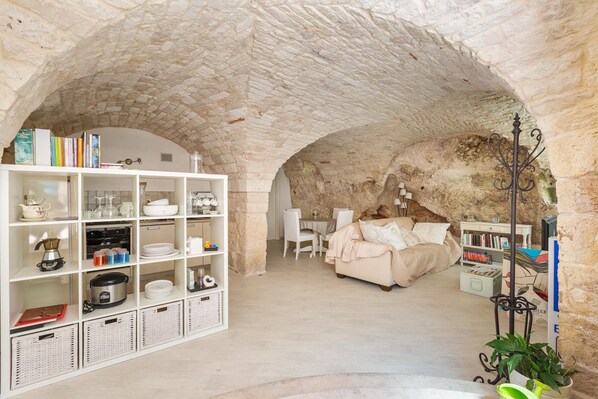A cozy room with a stone ceiling, a white bookshelf, a bed, and a dining area.
