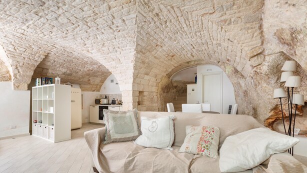 A room with a stone ceiling, a sofa with cushions, a bookshelf, and a lamp. - 2774 Casa Chianchizze by Barbarhouse (Ceglie Messapica)