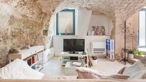 A cozy living room with a stone wall, a television, a bookshelf, and a comfortable seating area. - 2774 Casa Chianchizze by Barbarhouse (Ceglie Messapica)