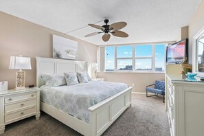 Una camera da letto con un letto, una ventola a soffitto, una cassettiera, una sedia e una finestra con vista.