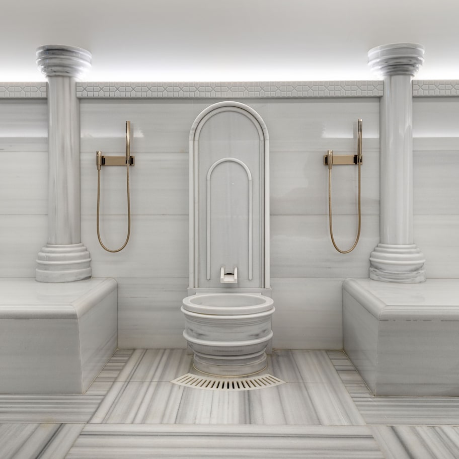 A modern bathroom with a freestanding toilet, two gold showerheads, and marble flooring.