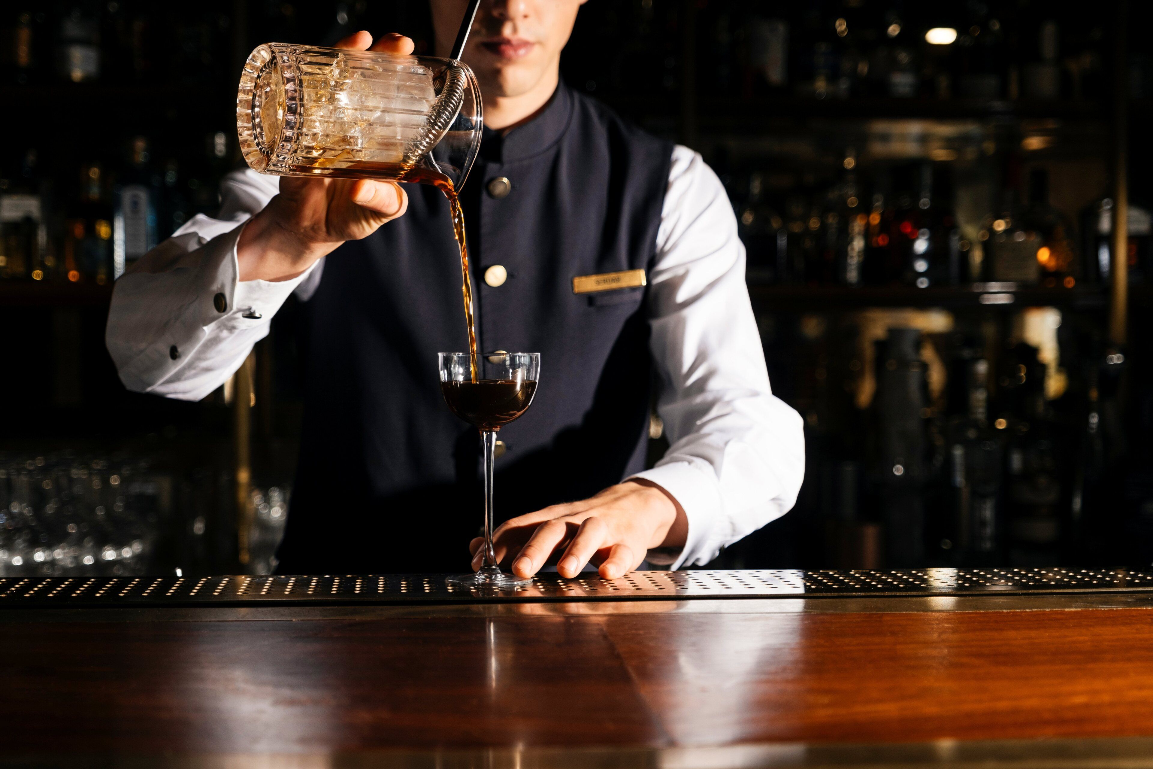 A bartender pouring a drink into a glass.
