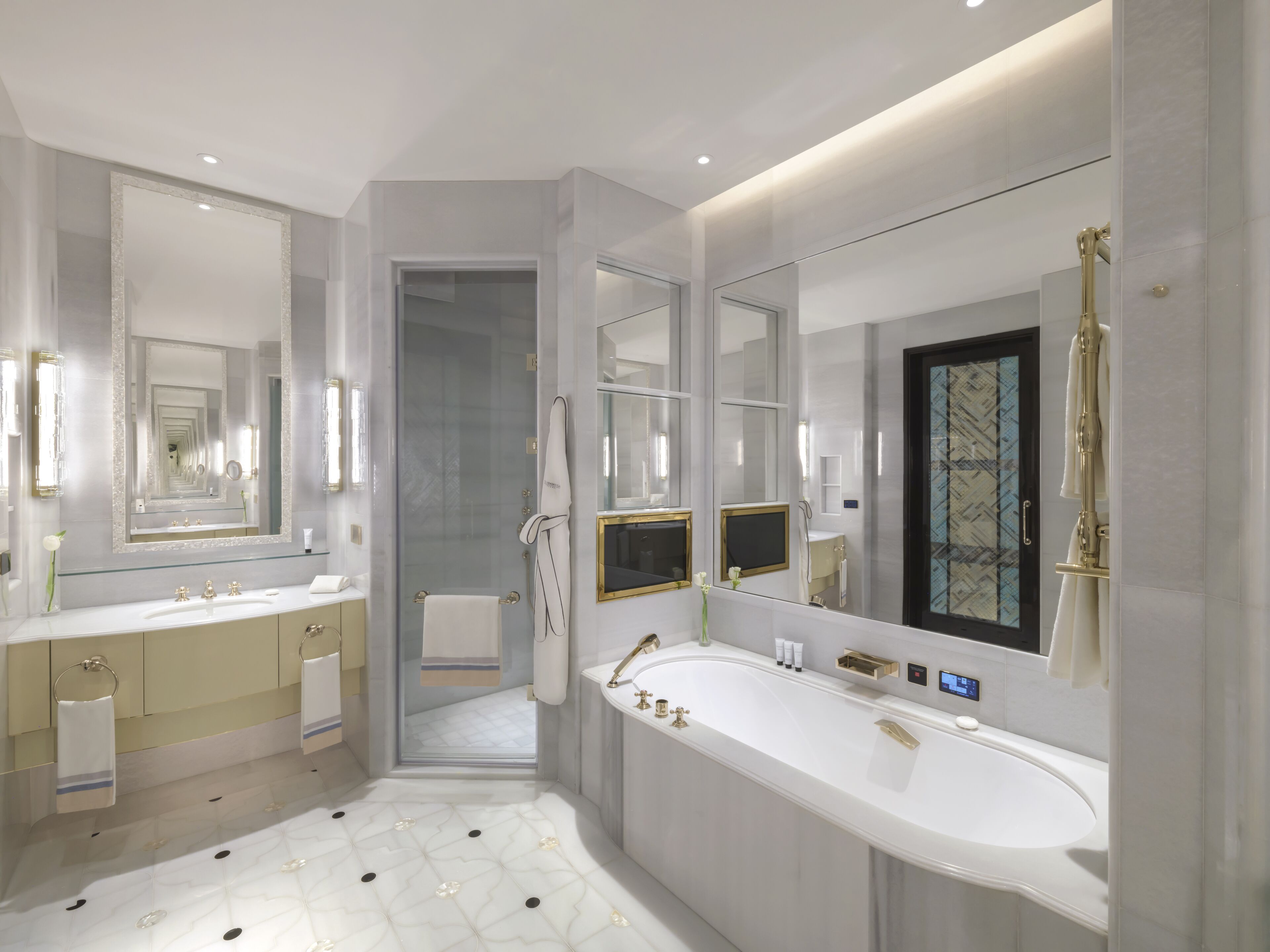 A modern bathroom with a large white bathtub, two sinks, and a walk-in shower.