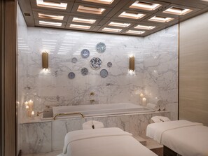 A modern bathroom with a marble wall, a bathtub, and two towels on a bench.