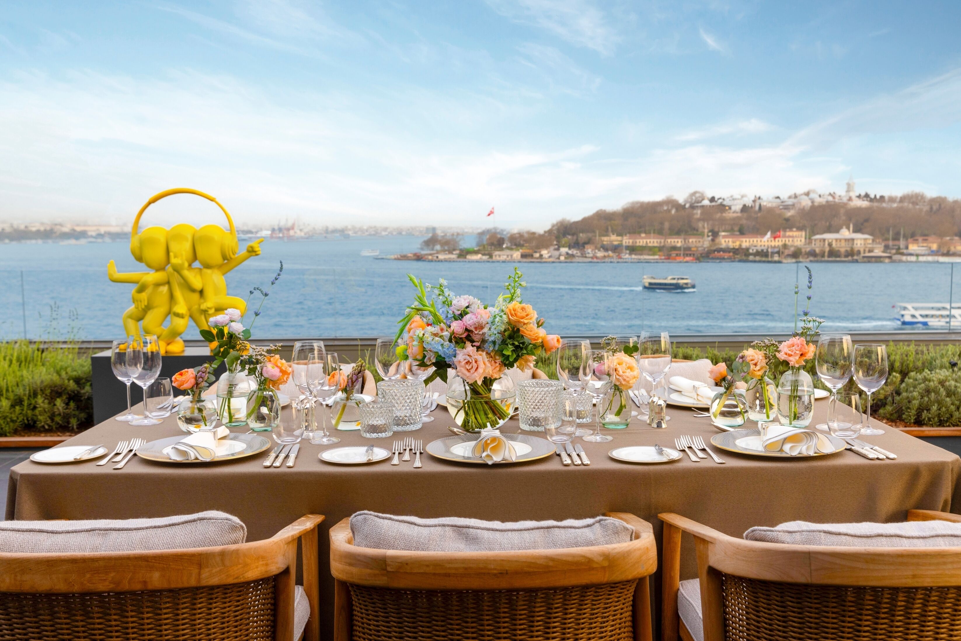 Mesa lista para una comida con vista a un cuerpo de agua y un paisaje urbano de fondo.