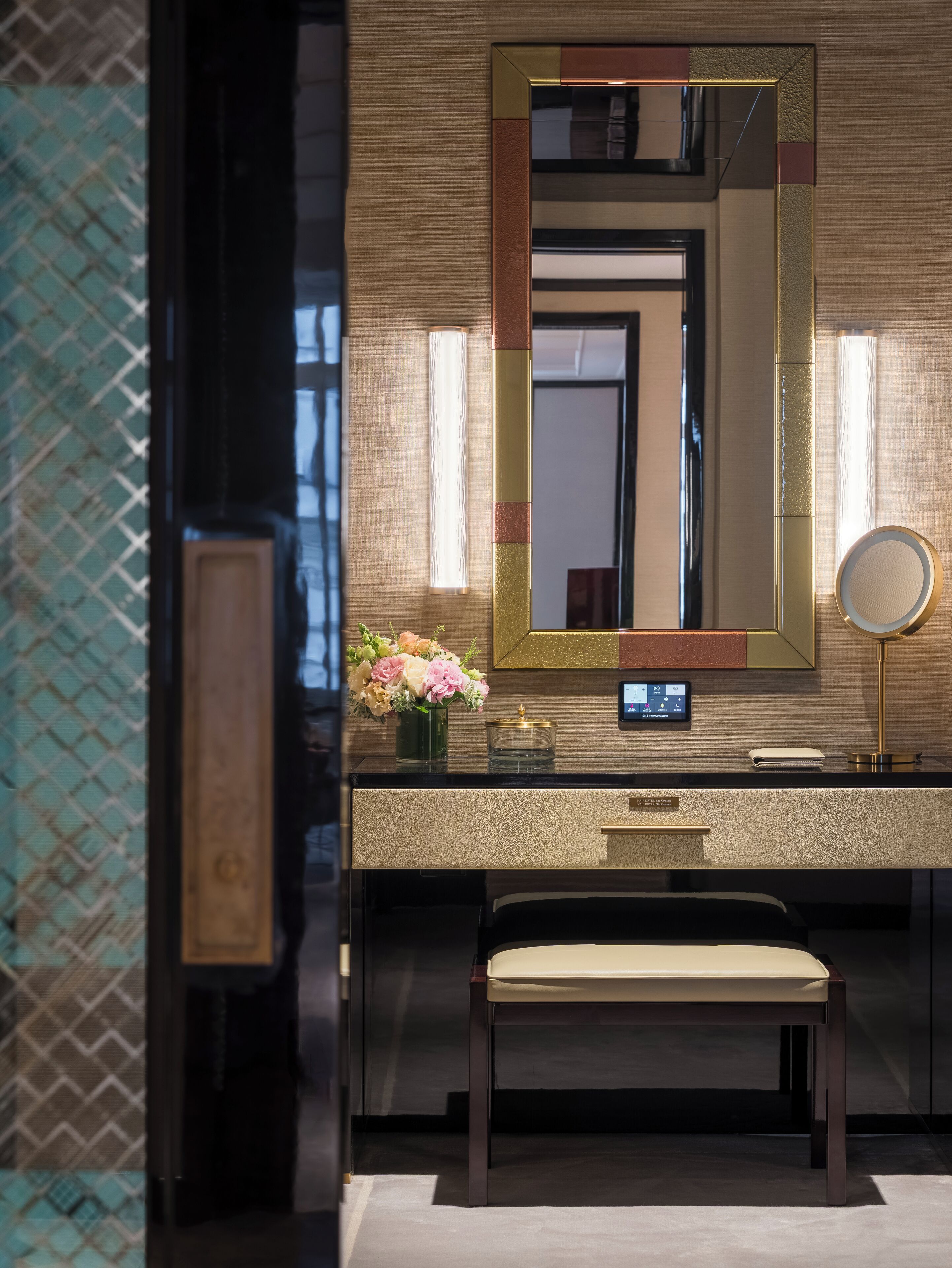 A modern bathroom with a large mirror, a vanity, a bench, and a vase of flowers.