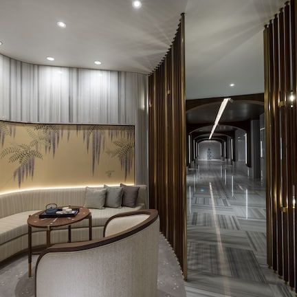A modern hotel lobby with a curved sofa, a small round table, and a decorative wall with hanging elements.