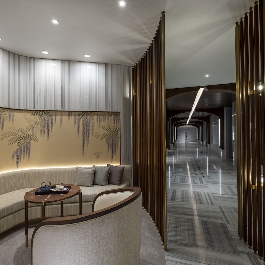 A modern hotel lobby with a curved sofa, a small round table, and a decorative wall with hanging elements.